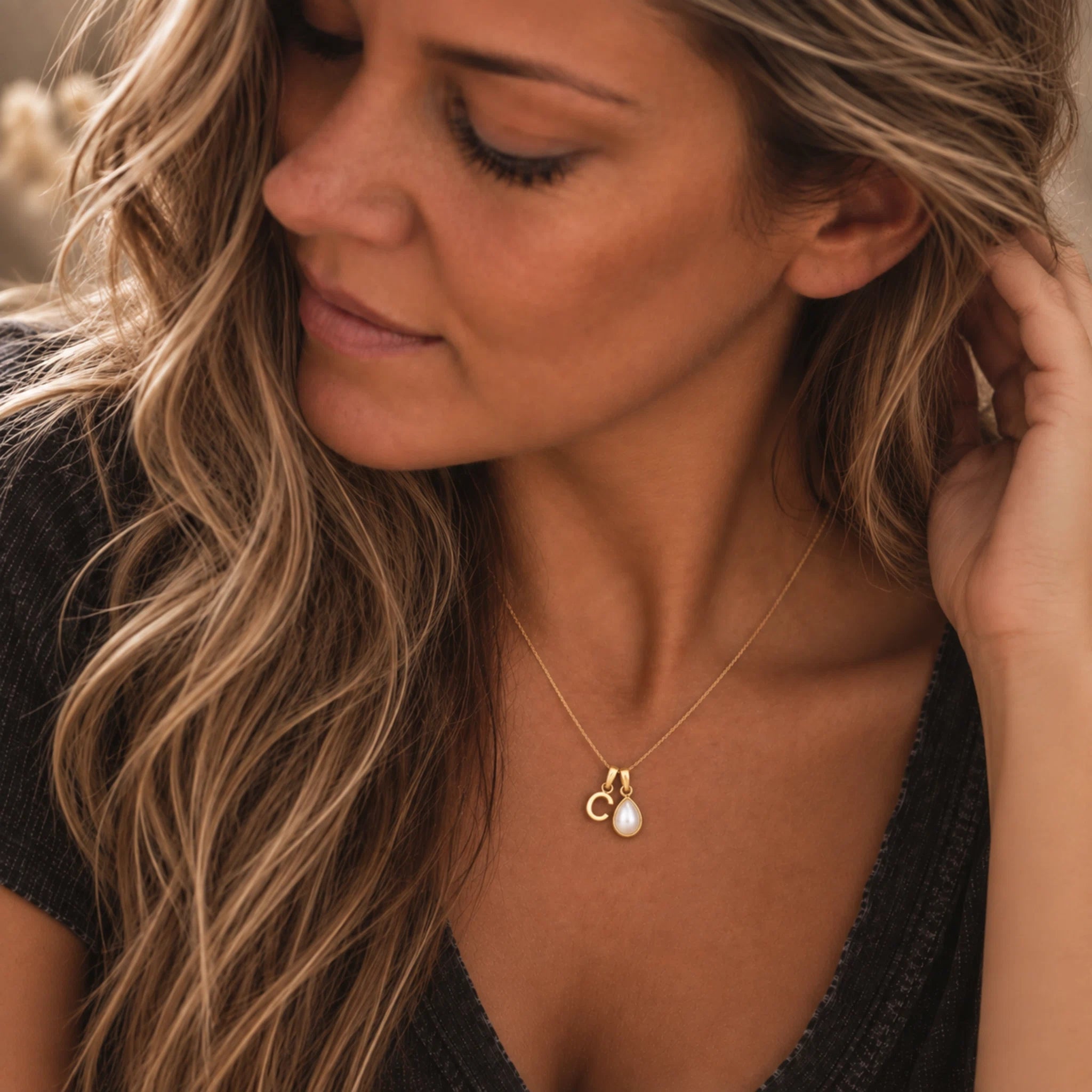 A close-up lifestyle shot of a woman wearing a delicate gold necklace with a double-ring pendant and a small white pearl, paired with a black top.