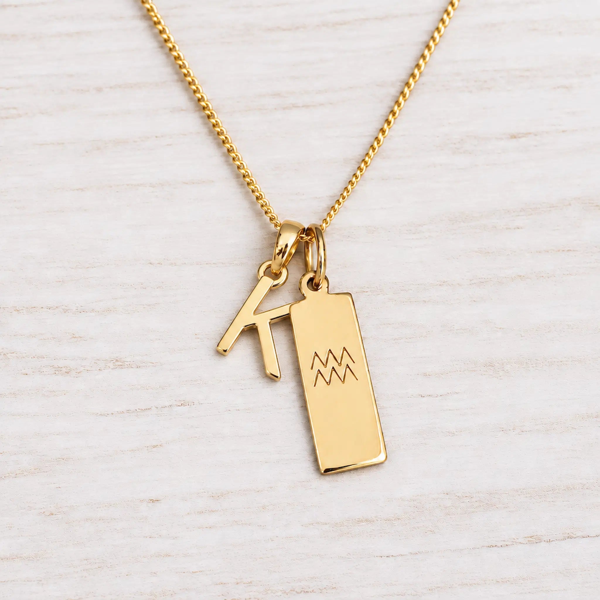 Gold Initial and Aquarius Zodiac Necklace with letter K pendant on light wood