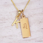 Gold initial and Leo zodiac necklace with a letter K pendant and engraved Leo bar on white wood, close-up