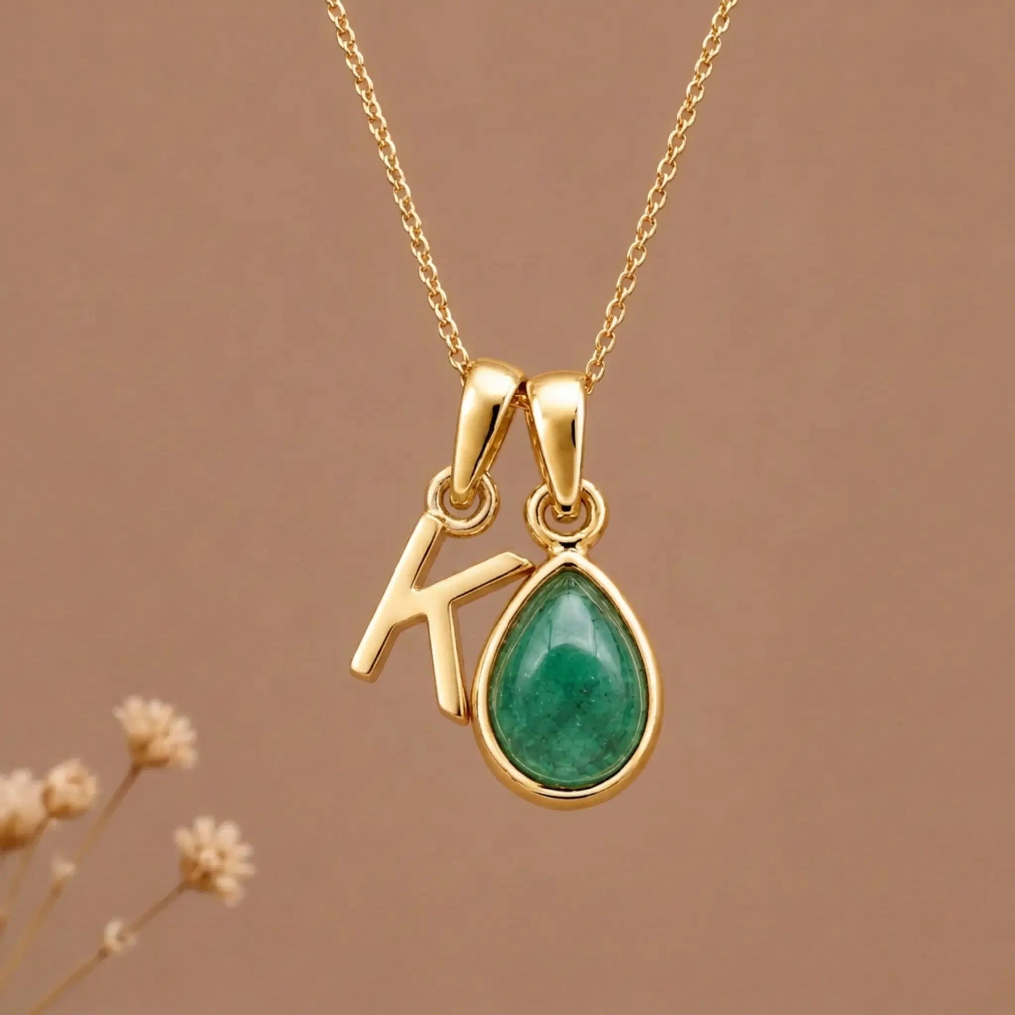 Gold Initial K and May Birthstone Emerald Necklace against a warm background