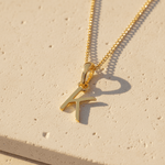 Gold necklace with a letter 'K' pendant on a beige surface