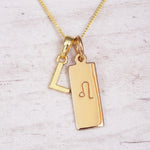 Gold initial and Leo zodiac necklace with a letter L pendant and engraved Leo bar on white wood, close-up