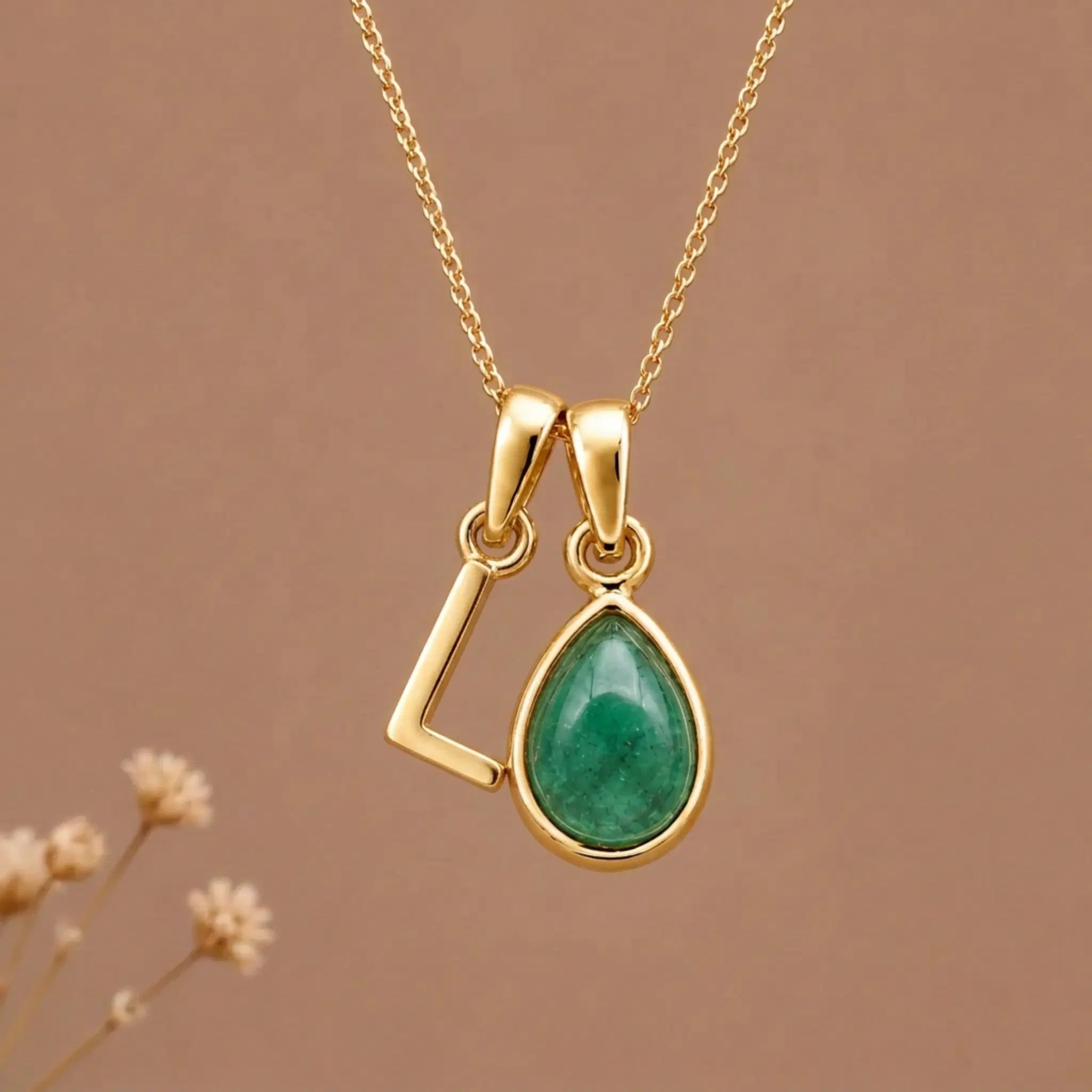 Gold Initial L and May Birthstone Emerald Necklace against a warm background
