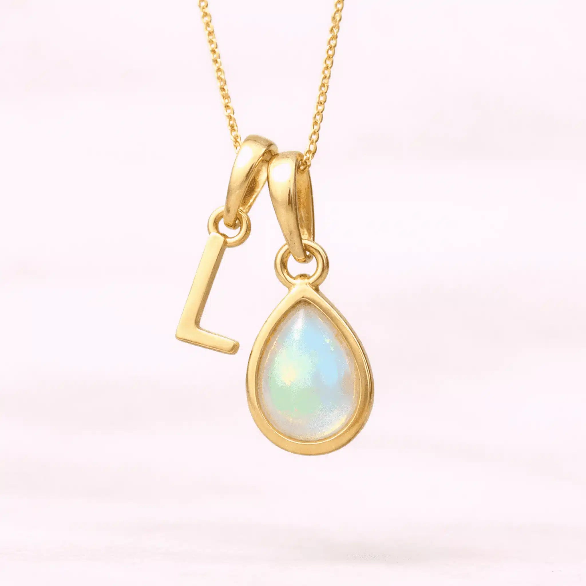 Gold October birthstone necklace with a pear-shaped natural opal pendant and letter 'L' charm with a light background.
