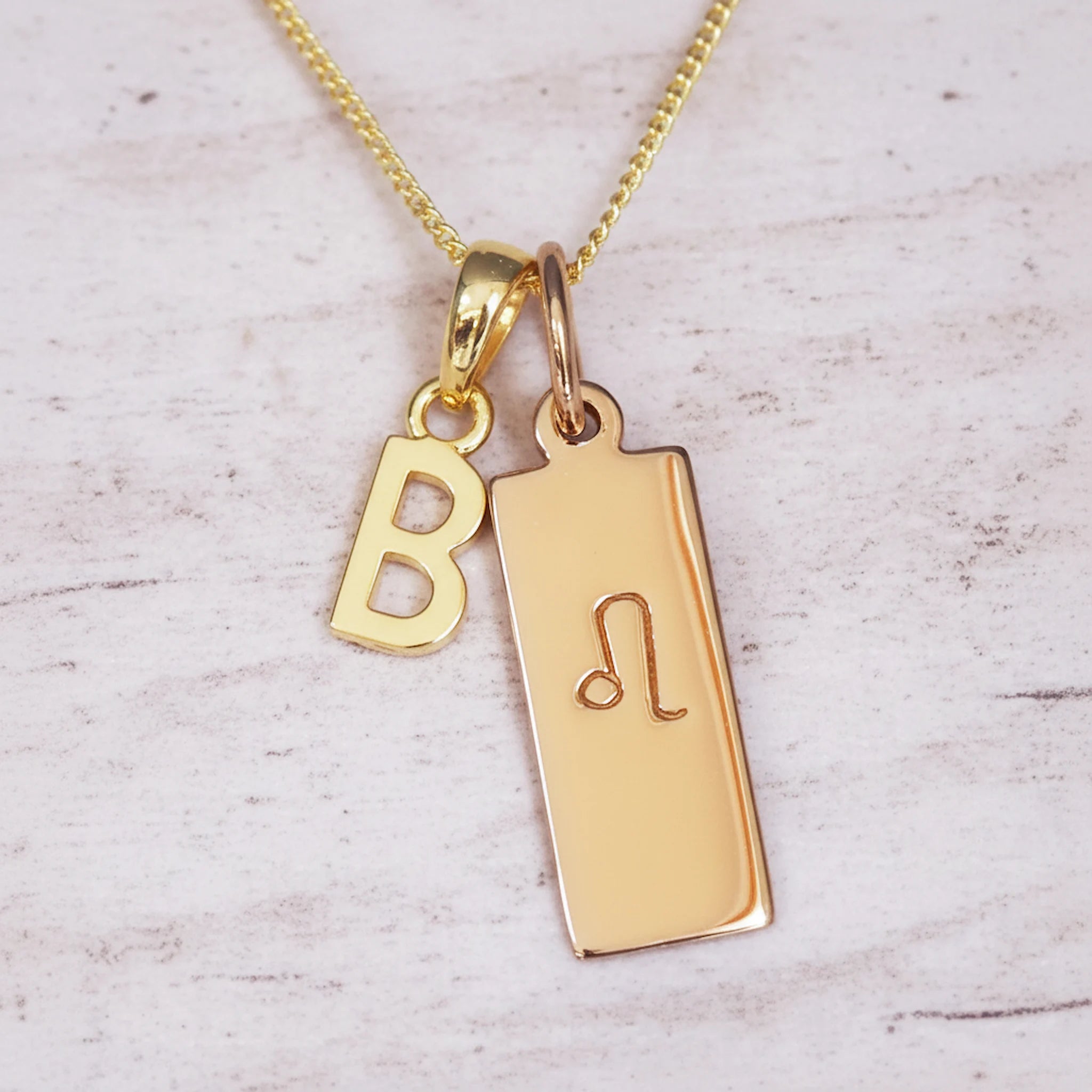 Gold necklace with 'B' initial pendant and leo zodiac star sign pendant on a light wooden background