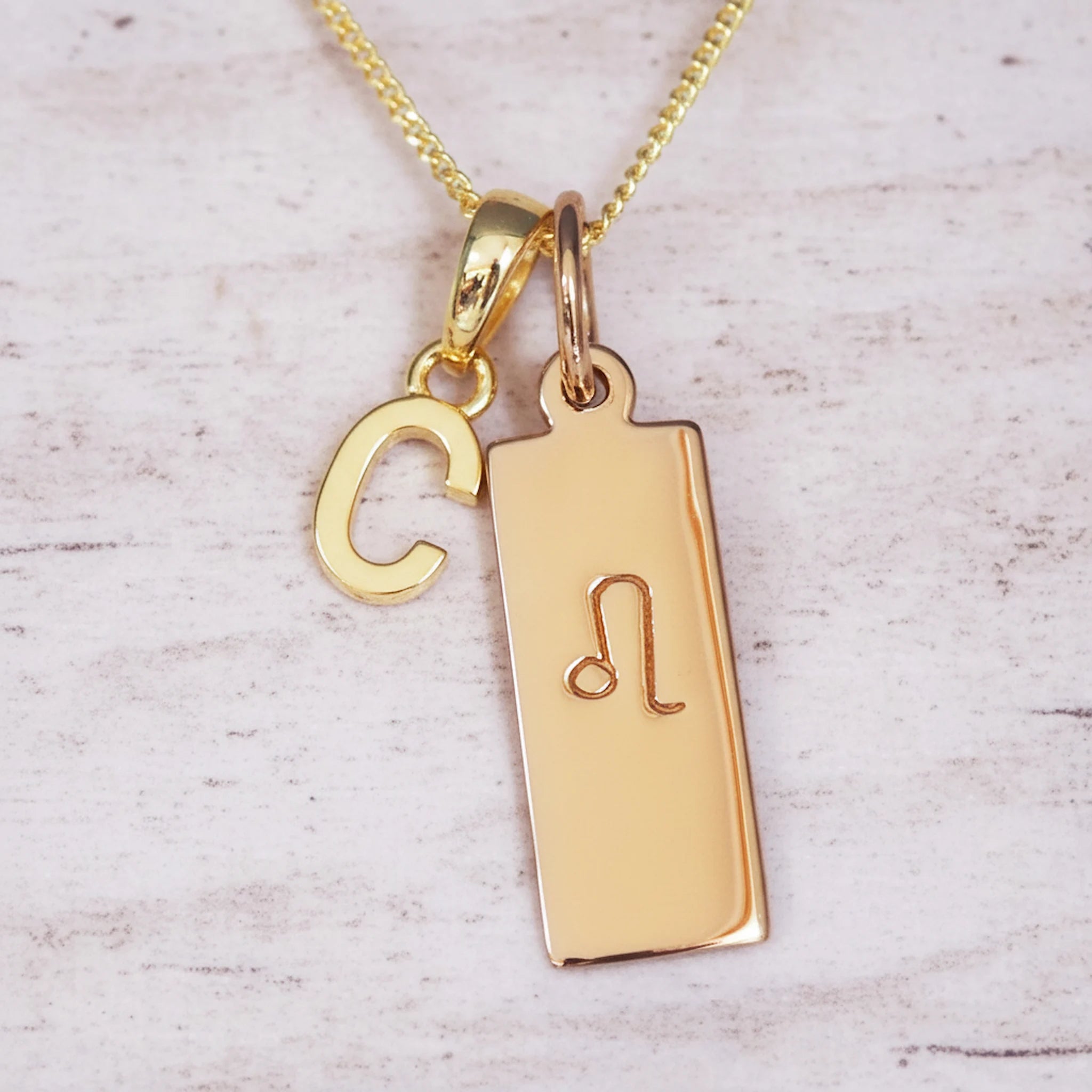 Gold necklace with 'C' initial pendant and leo zodiac star sign pendant on a light wooden background