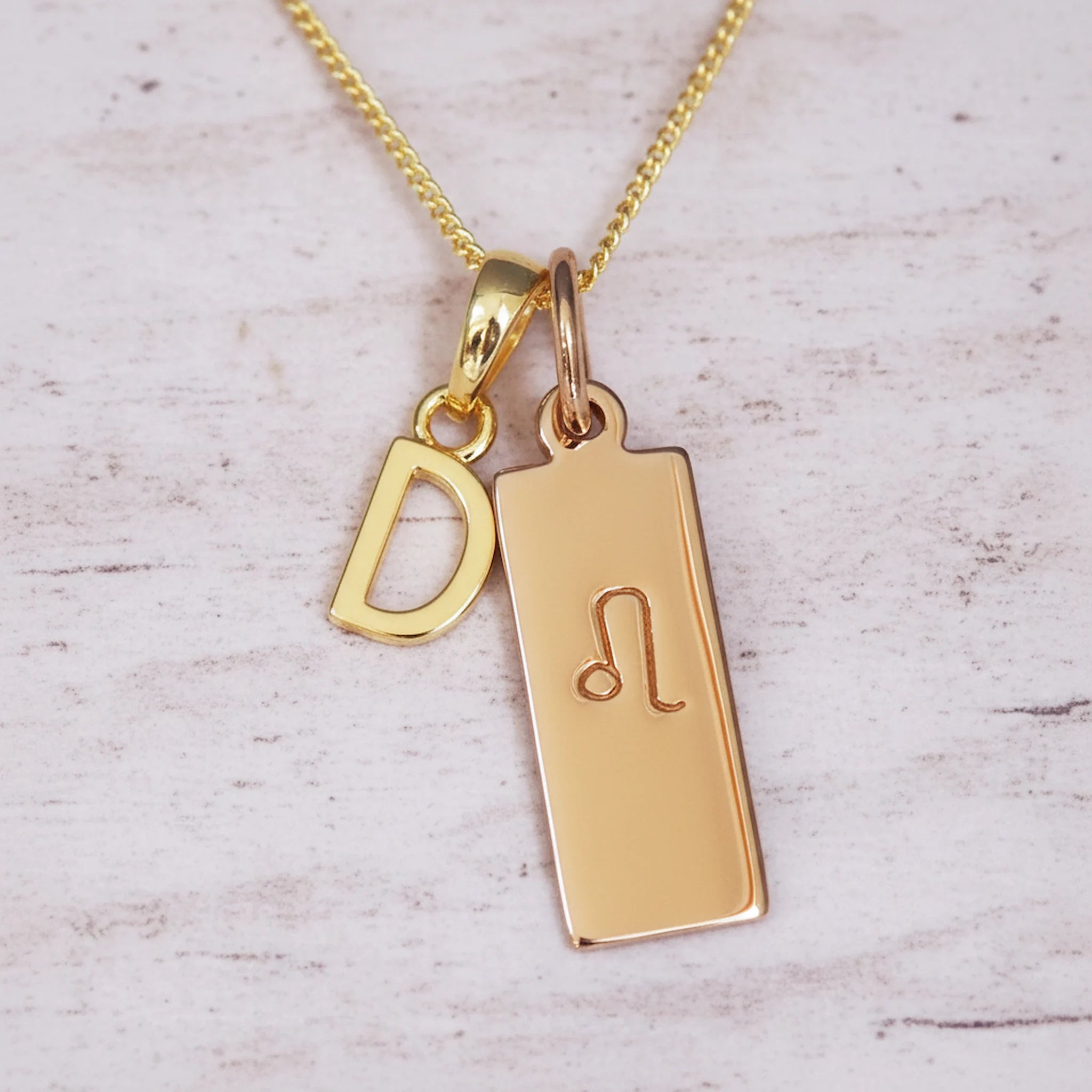 Gold necklace with 'D' initial pendant and leo zodiac star sign pendant on a light wooden background