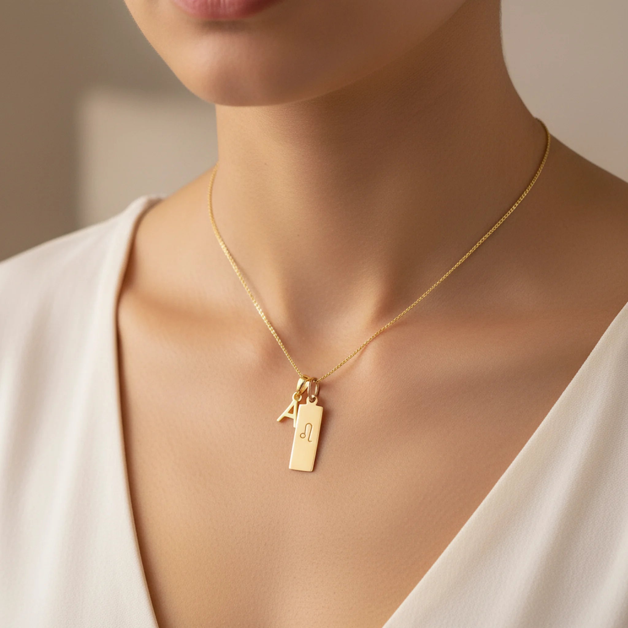 Model wearing a gold Leo zodiac necklace with an initial charm and polished rectangular bar tag engraved with the Leo glyph