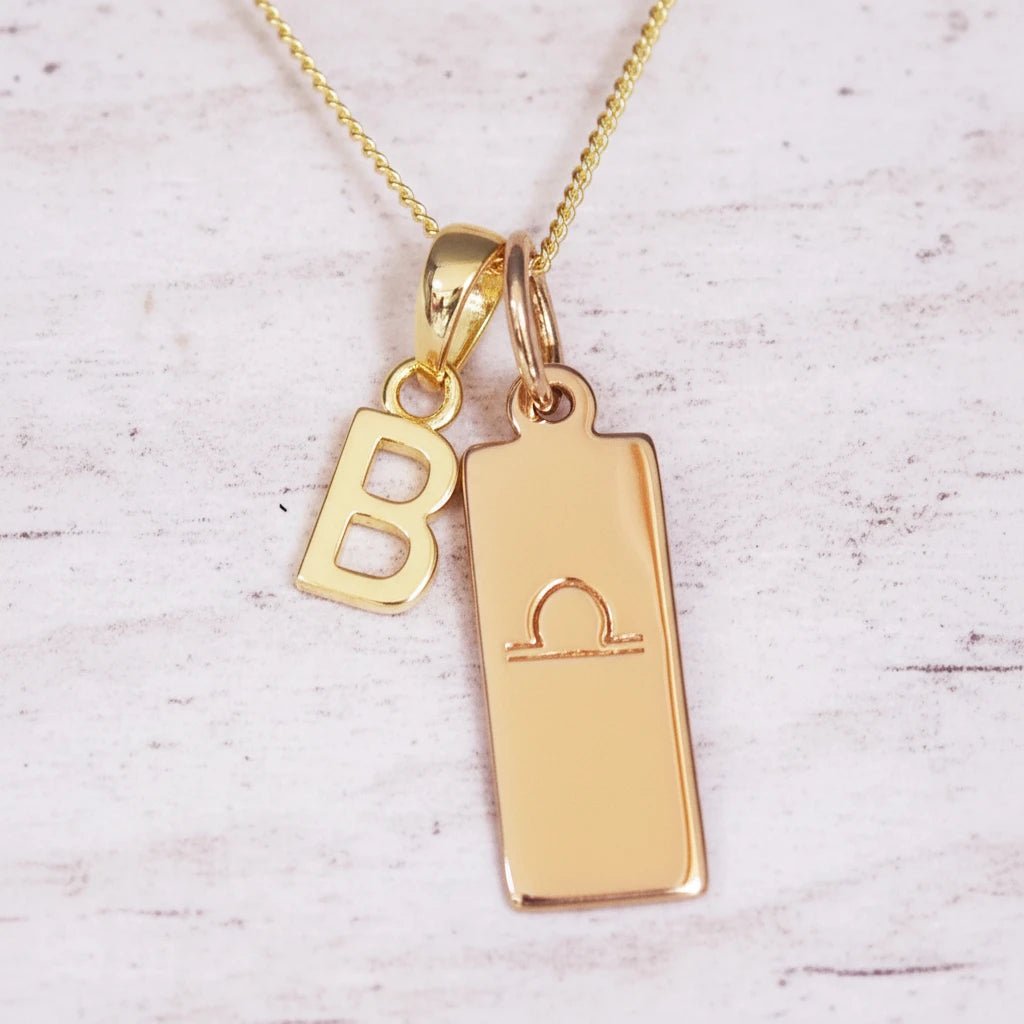Gold necklace with 'B' pendant and libra zodiac sign on a light background