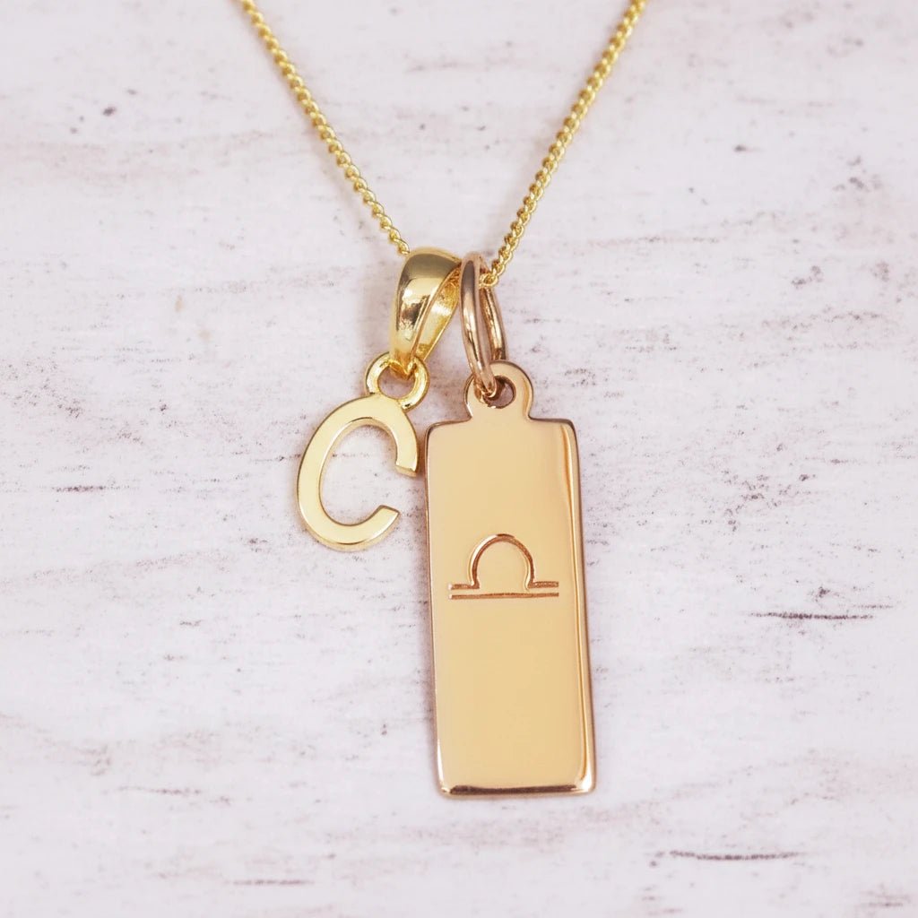 Gold necklace with 'C' pendant and libra zodiac sign on a light background