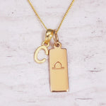 Gold necklace with 'C' pendant and libra zodiac sign on a light background