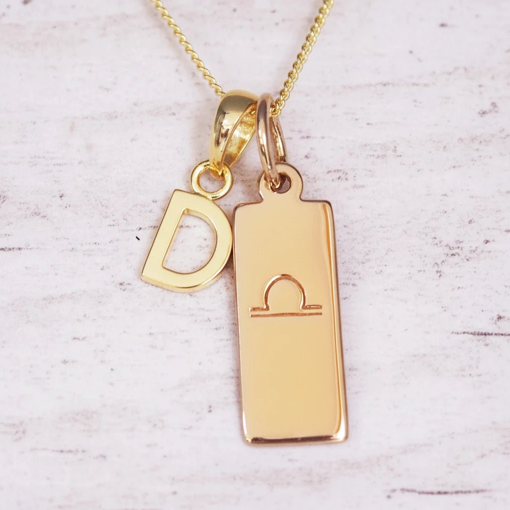 Gold necklace with 'D' pendant and libra zodiac sign on a light background