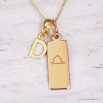 Gold necklace with 'D' pendant and libra zodiac sign on a light background
