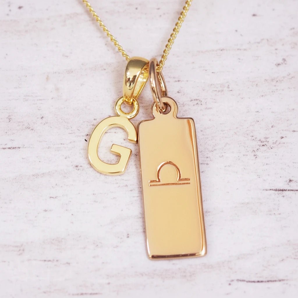 Gold necklace with 'G' pendant and libra zodiac sign on a light background