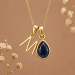 Gold Initial M Pendant and September birthstone Natural Sapphire Necklace against a warm background