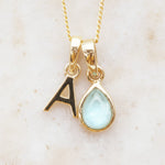 Gold necklace with a letter 'A' pendant and a teardrop-shaped gemstone on a light background