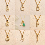 Collection of gold fine chain necklaces with uppercase gold letter pendants  on a beige background with B, C, D, E, A, F, G, H, I initials as options for a May Birthstone Emerald Necklace.