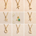 Collection of gold fine chain necklaces with uppercase gold letter pendants  on a beige background, J, K, L, M, A, N, O, P, Q initials as options for a May Birthstone Emerald Necklace.