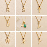 Collection of gold fine chain necklaces with uppercase gold letter pendants  on a beige background, S, T, Y, A, V, W, X, Y initials as options for a May Birthstone Emerald Necklace.