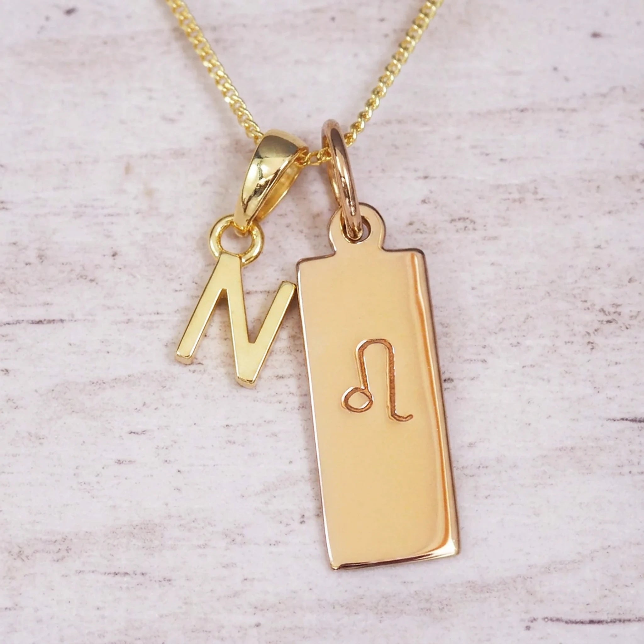 Gold initial and Leo zodiac necklace with a letter N pendant and engraved Leo bar on white wood, close-up