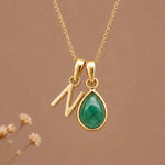 Gold Initial N and May Birthstone Emerald Necklace against a warm background