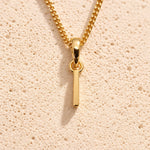 Personalised gold initial letter pendant necklace with polished uppercase I pendant on a fine cable chain in 9k gold plated sterling silver against a textured beige stone background