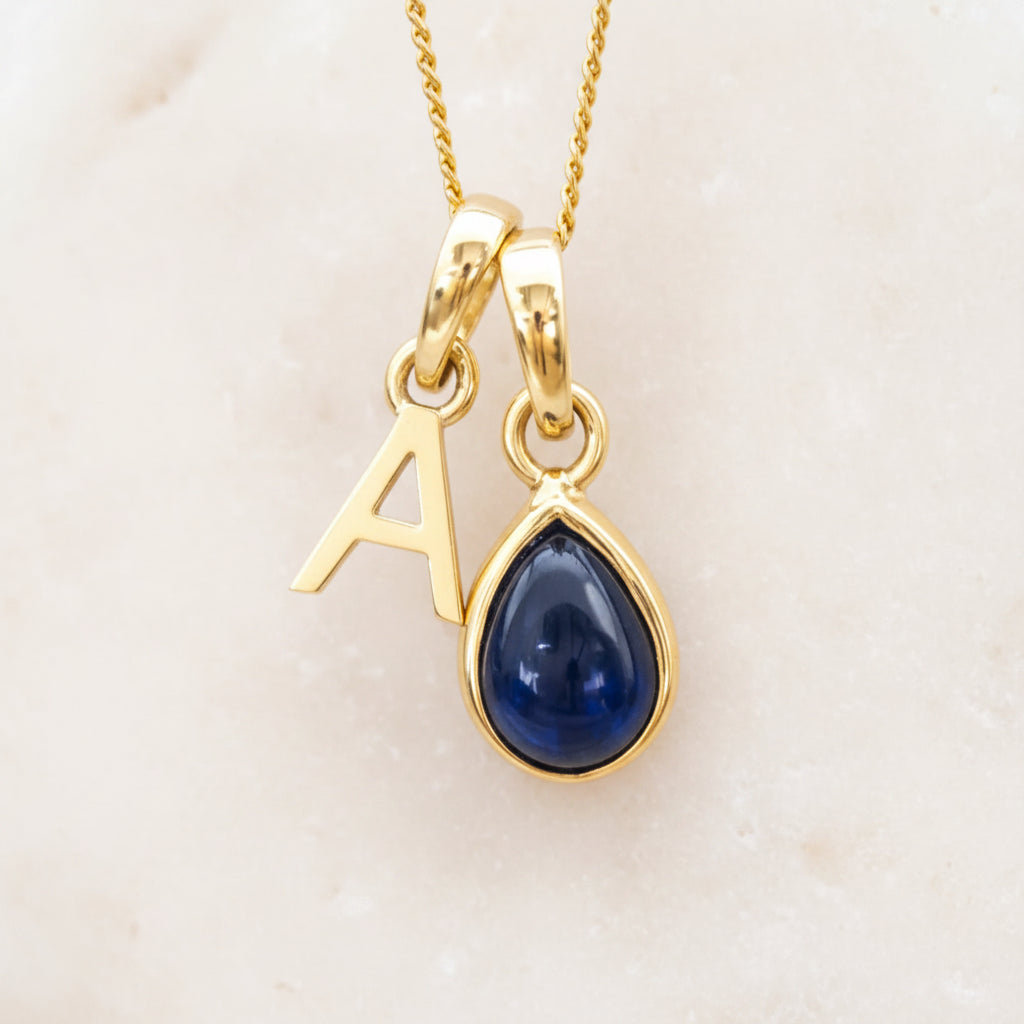 Gold September birthstone necklace with a blue sapphire teardrop pendant and letter 'A' charm