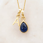 Gold September birthstone necklace with a blue sapphire teardrop pendant and letter 'A' charm