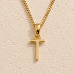 Polished gold initial pendant necklace with uppercase T charm on a fine link chain against beige stone