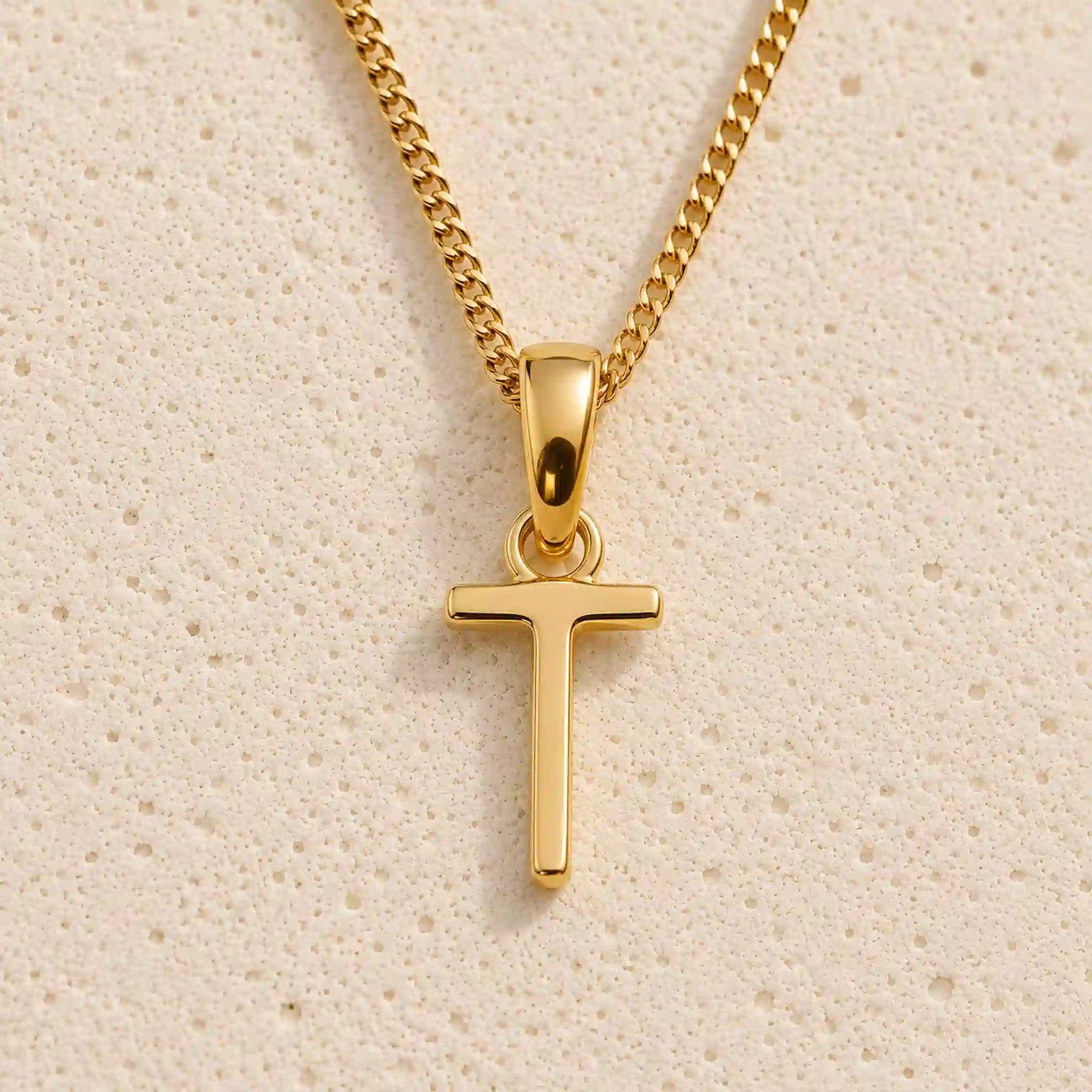 Polished gold initial pendant necklace with uppercase T charm on a fine link chain against beige stone