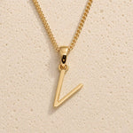 Polished gold initial pendant necklace with uppercase V charm on a fine link chain against beige stone