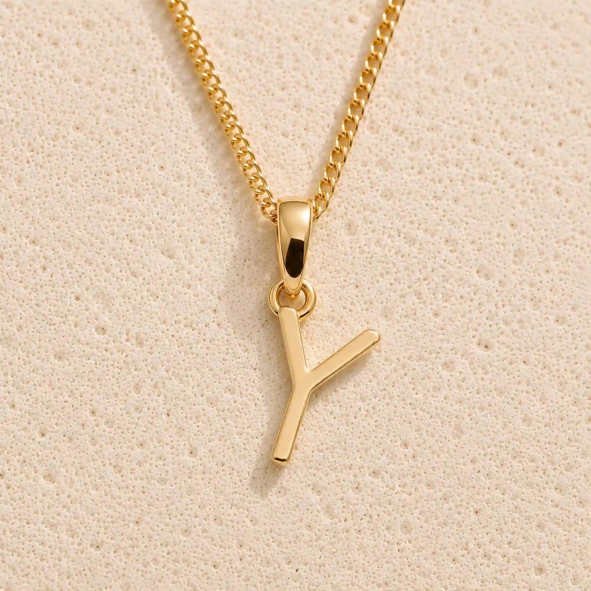Polished gold initial pendant necklace with uppercase Y charm on a fine link chain against beige stone