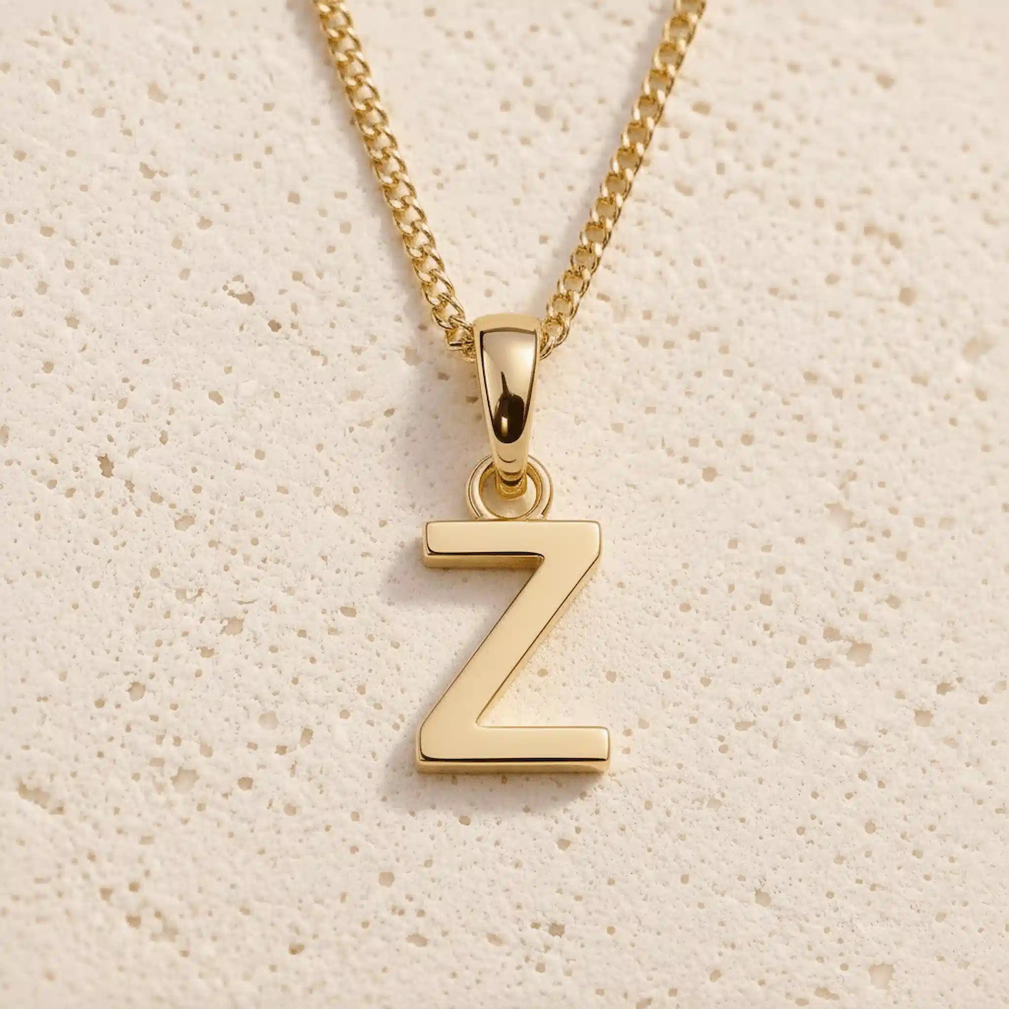 Polished gold initial pendant necklace with uppercase Z charm on a fine link chain against beige stone as a personalised gold letter pendant for a Taurus Zodiac Necklace.