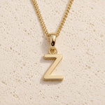 Polished gold initial pendant necklace with uppercase Z charm on a fine link chain against beige stone