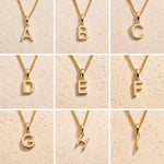 3 x 3 grid showing gold initial necklace charms A, B, C, D, E, F, G, H and I on fine cable chains against a beige stone background, showing personalised letter options for the Leo zodiac necklace