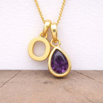 Gold necklace with a purple teardrop pendant on a wooden surface