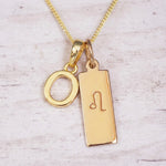 Gold initial and Leo zodiac necklace with a letter O pendant and engraved Leo bar on white wood, close-up