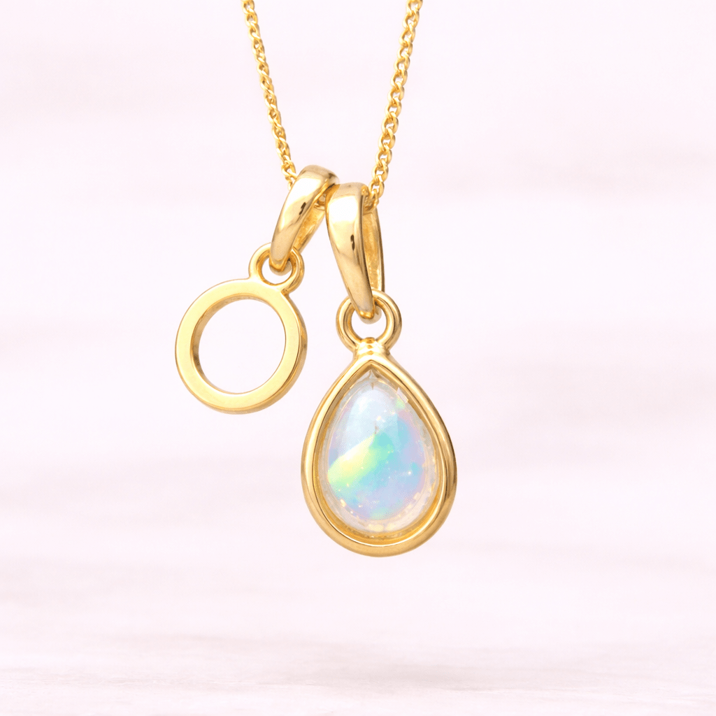 Gold necklace with a 'O' initial pendant and a teardrop-shaped opal pendant on a light pink background