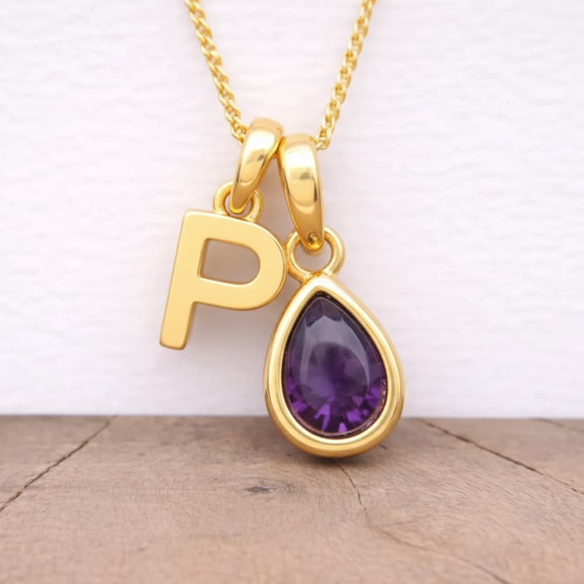 Gold necklace with a 'P' pendant and purple amethyst gemstone on a wooden surface.