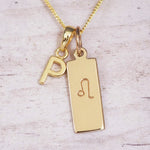 Gold initial and Leo zodiac necklace with a letter P pendant and engraved Leo bar on white wood, close-up
