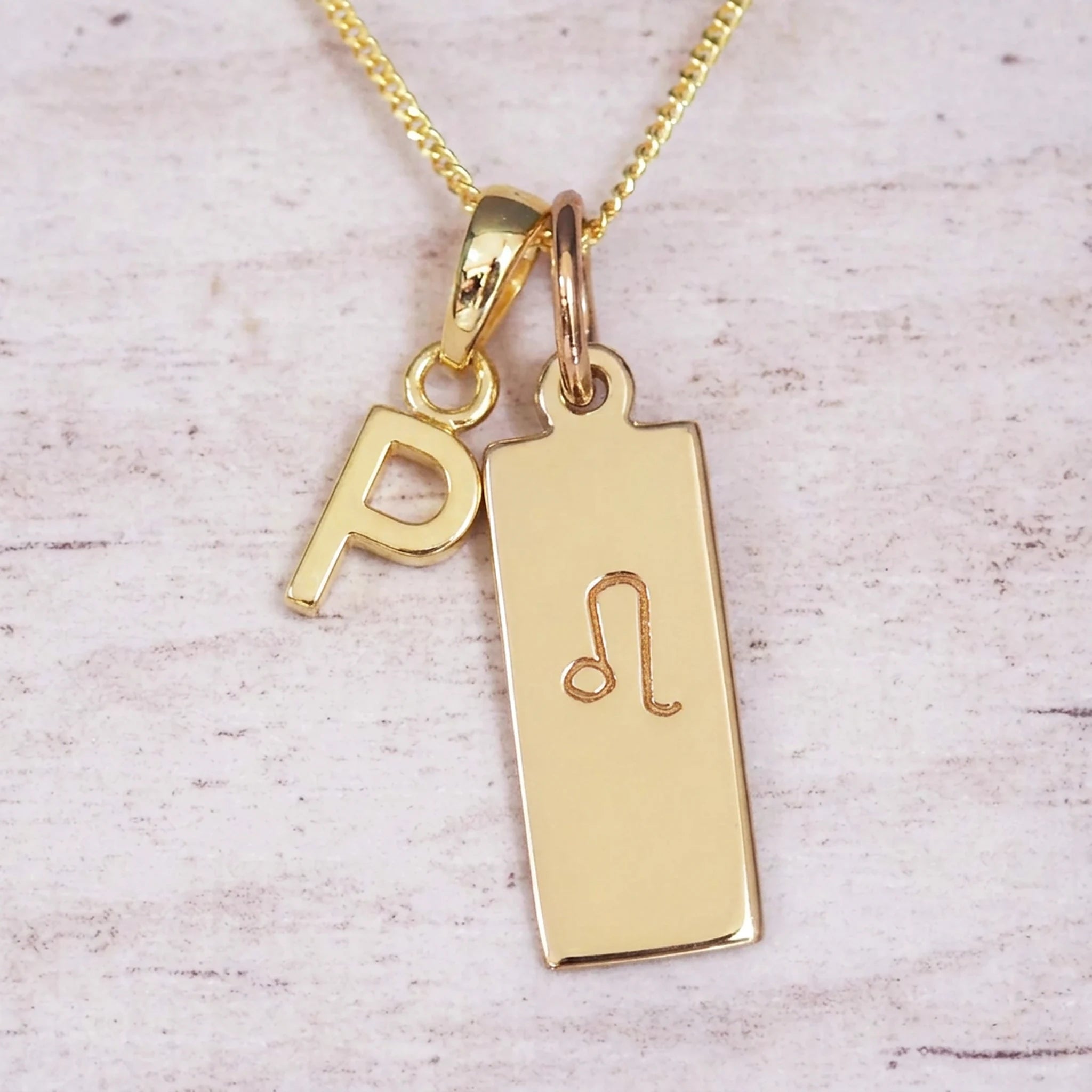 Gold initial and Leo zodiac necklace with a letter P pendant and engraved Leo bar on white wood, close-up