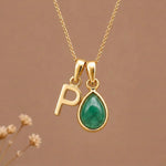 Gold Initial P and May Birthstone Emerald Necklace against a warm background