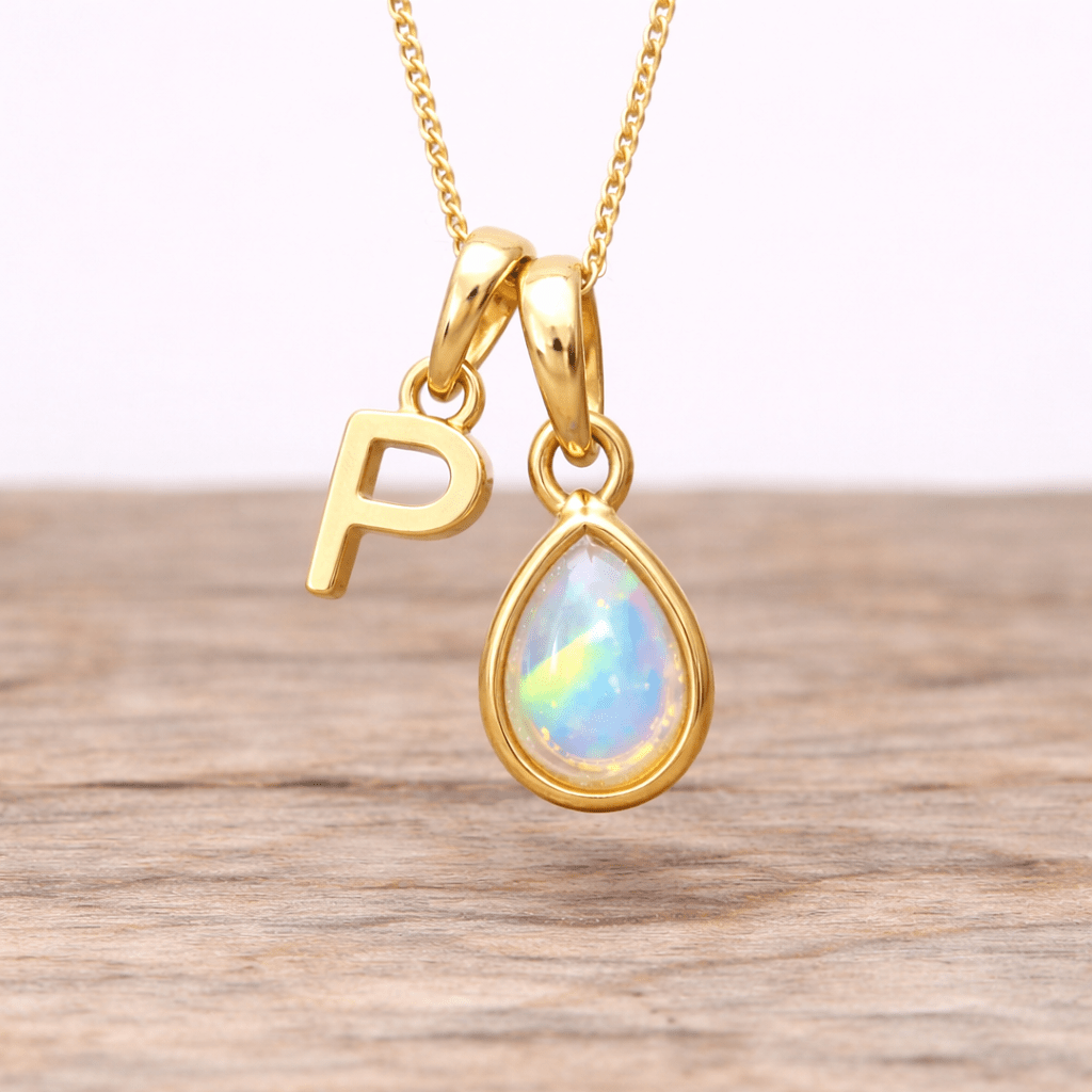 Gold necklace with a teardrop-shaped opal pendant and a letter 'P' charm on a wooden surface.