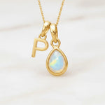 Gold October birthstone necklace with a pear-shaped natural opal pendant and letter 'P' charm with a light background.