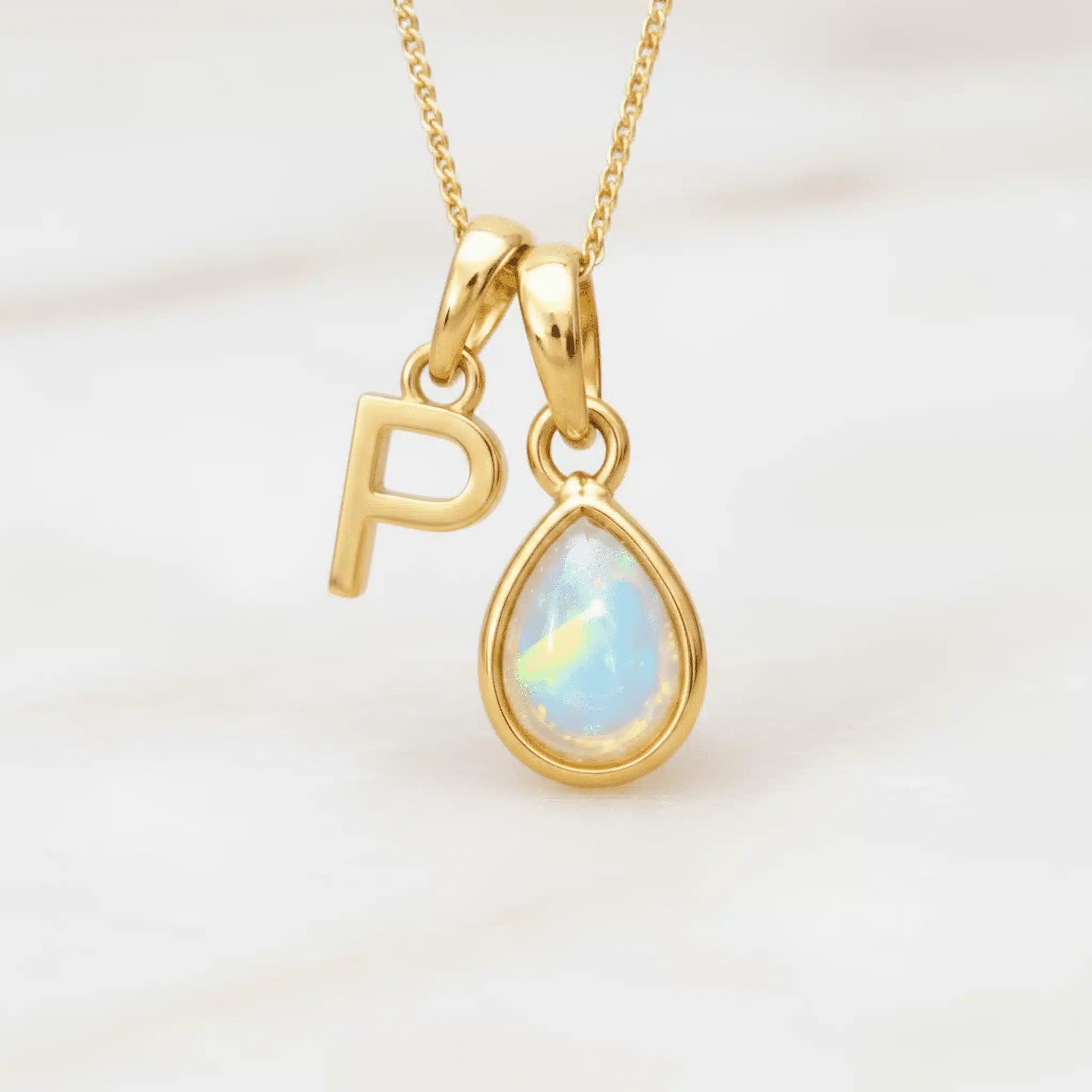 Gold October birthstone necklace with a pear-shaped natural opal pendant and letter 'P' charm with a light background.