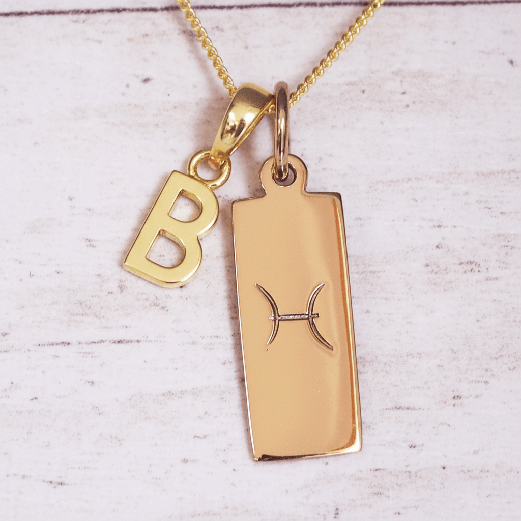 Gold necklace with 'B' pendant and pisces zodiac sign on a light wooden background