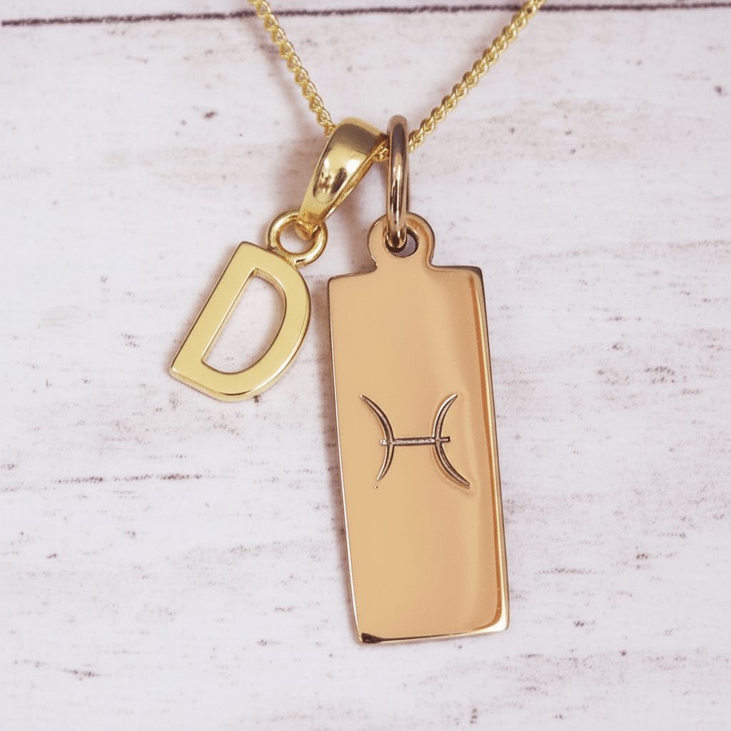 Gold necklace with a pisces zodiac pendant and 'D' charm on a light wooden surface