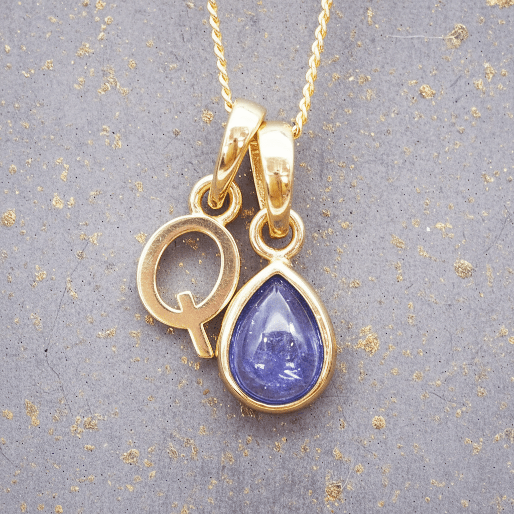 Gold necklace with a 'Q' initial pendant with a purple december birthstone natural tanzanite gemstone pendant on a textured gray background
