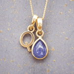 Gold necklace with a 'Q' initial pendant with a purple december birthstone natural tanzanite gemstone pendant on a textured gray background