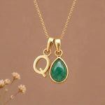 Gold Initial Q and May Birthstone Emerald Necklace against a warm background